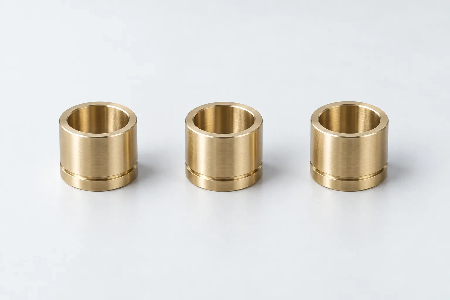 Three turned brass bushings stand in a row with their bores and circumferential grooves visible.